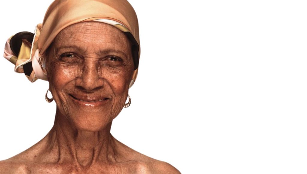 An older woman wearing an orange headscarf and gold hoop earrings, smiling.